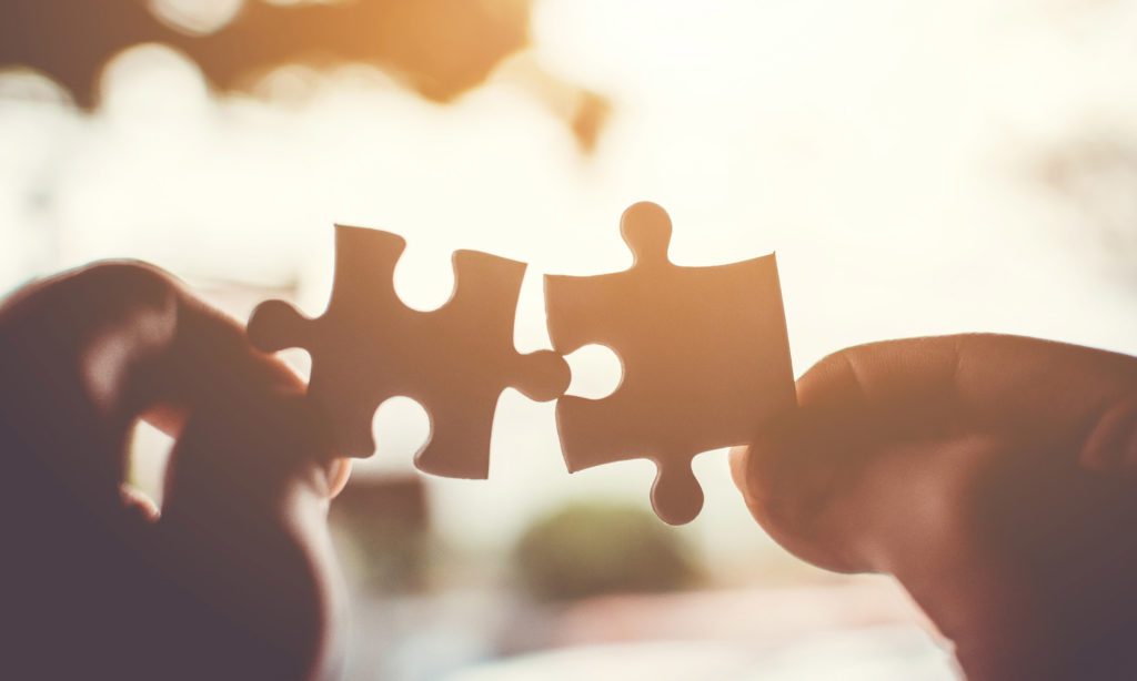 Two hands each hold a jigsaw puzzle piece, bringing them together